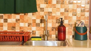 A kitchen with a tiled backsplash, a stainless steel sink, a red soap dispenser, a green basket, and a red utensil holder.