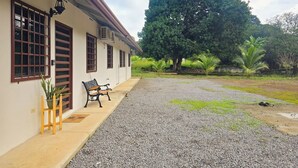 A building with a gravel driveway, a bench, and a large tree in the background.