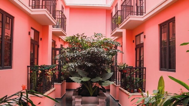 Un bâtiment rose doté d’un jardin central, de balcons et de plantes en pot.