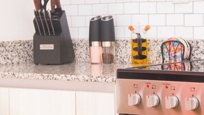 Un plan de travail de cuisine avec un range-couteaux, une machine à café, un récipient à épices et une plaque de cuisson dotée de boutons de contrôle.