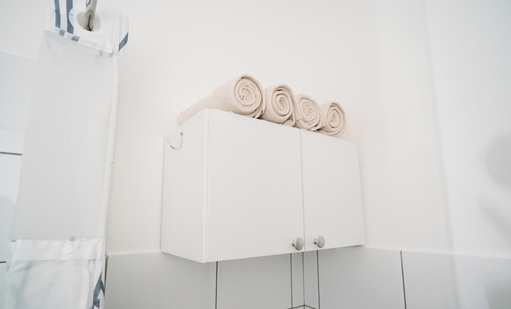 Un meuble blanc sur lequel sont pliés des serviettes, un rideau de douche et un mur recouvert de carreaux blancs.