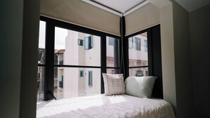 A bedroom with a bed, pillows, and a view of buildings through large windows. - The Glow Stay | Elegant and Modern | @SantaAna (Panama City)