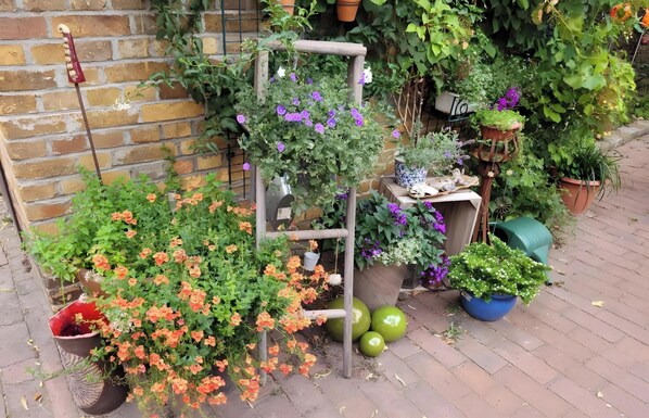 Ein Garten mit verschiedenen Blumentöpfen, Blumen, einem Holzzimmer und einer Backsteinmauer.