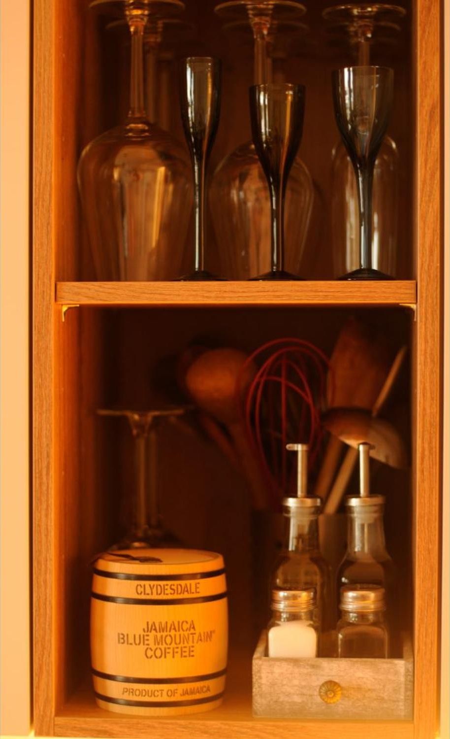 A wooden cabinet with shelves containing glassware and a jar of Jamaica Blue Mountain coffee.