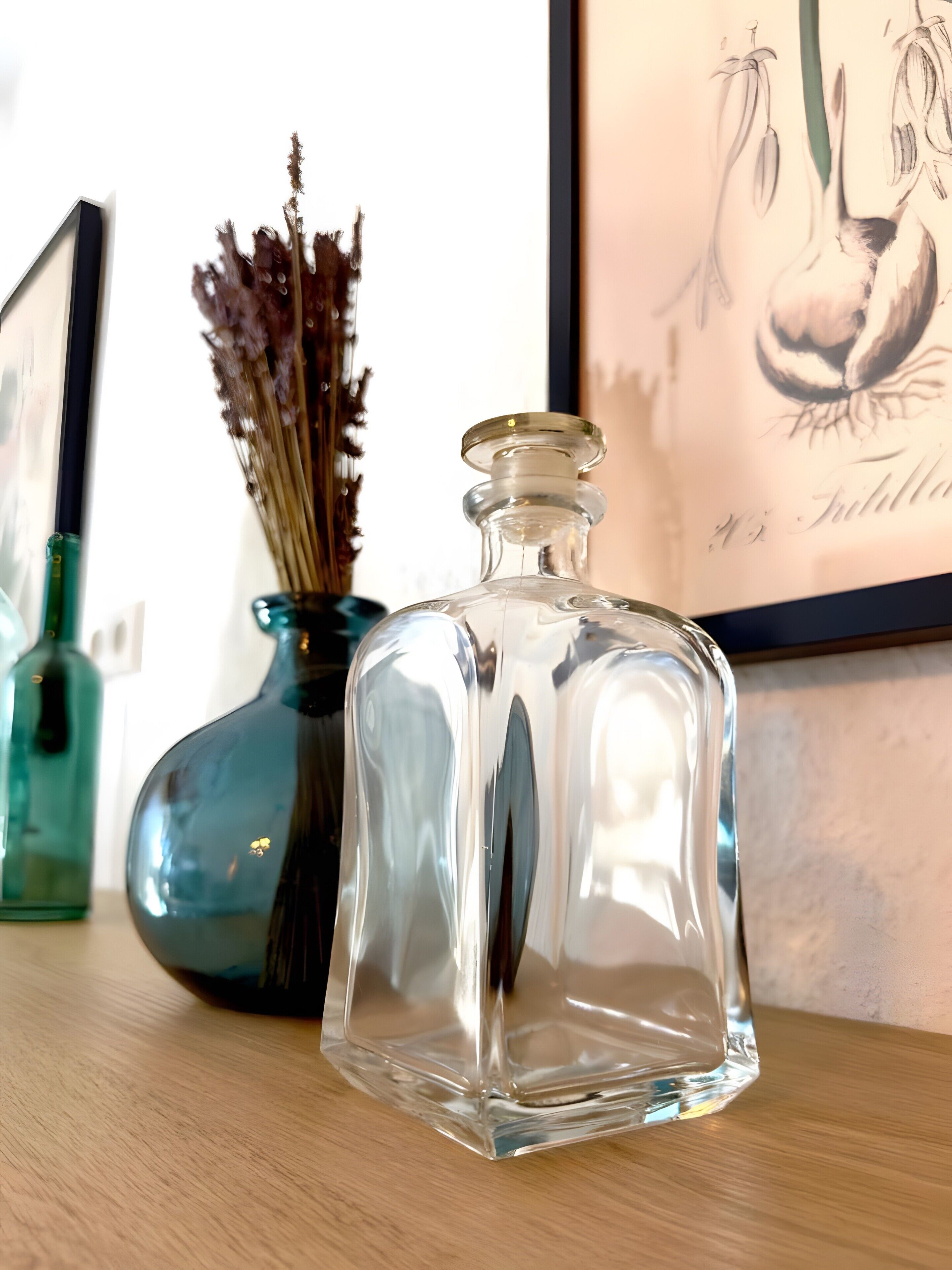 Een heldere glazen fles met een smalle hals en een breder voetje, geplaatst op een houten ondergrond.