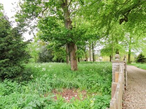 A pathway leading through a lush garden with a stone wall on one side and a tree-lined path on the other. - The Gardener's Cottage, Low Hall (Scarborough)