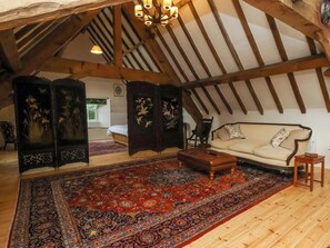 An attic room with a high ceiling, exposed wooden beams, a sofa, a small table, and a large ornate rug. - The Gardener's Cottage, Low Hall (Scarborough)