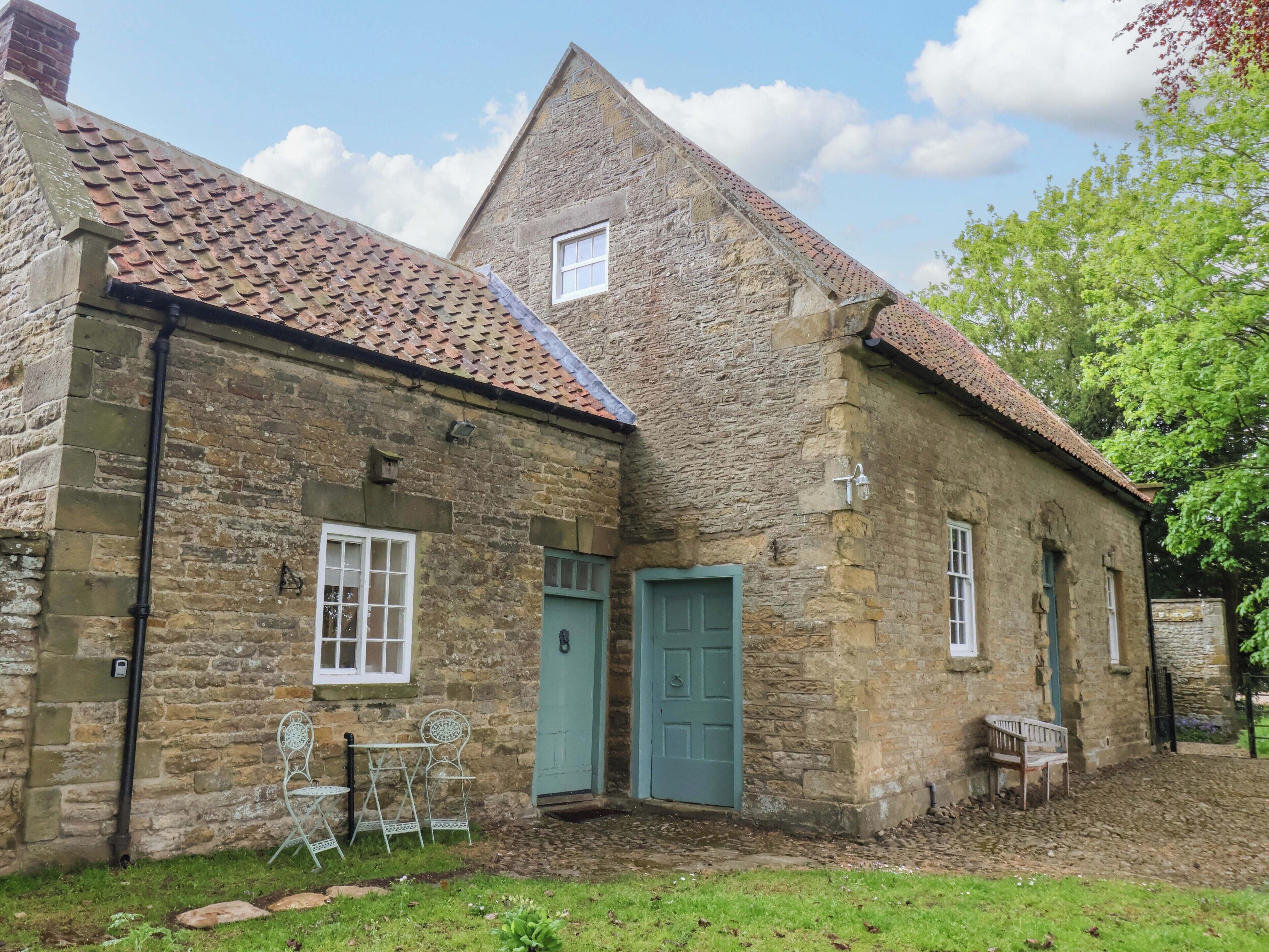 A stone building with a tiled roof, a green door, and a small window.