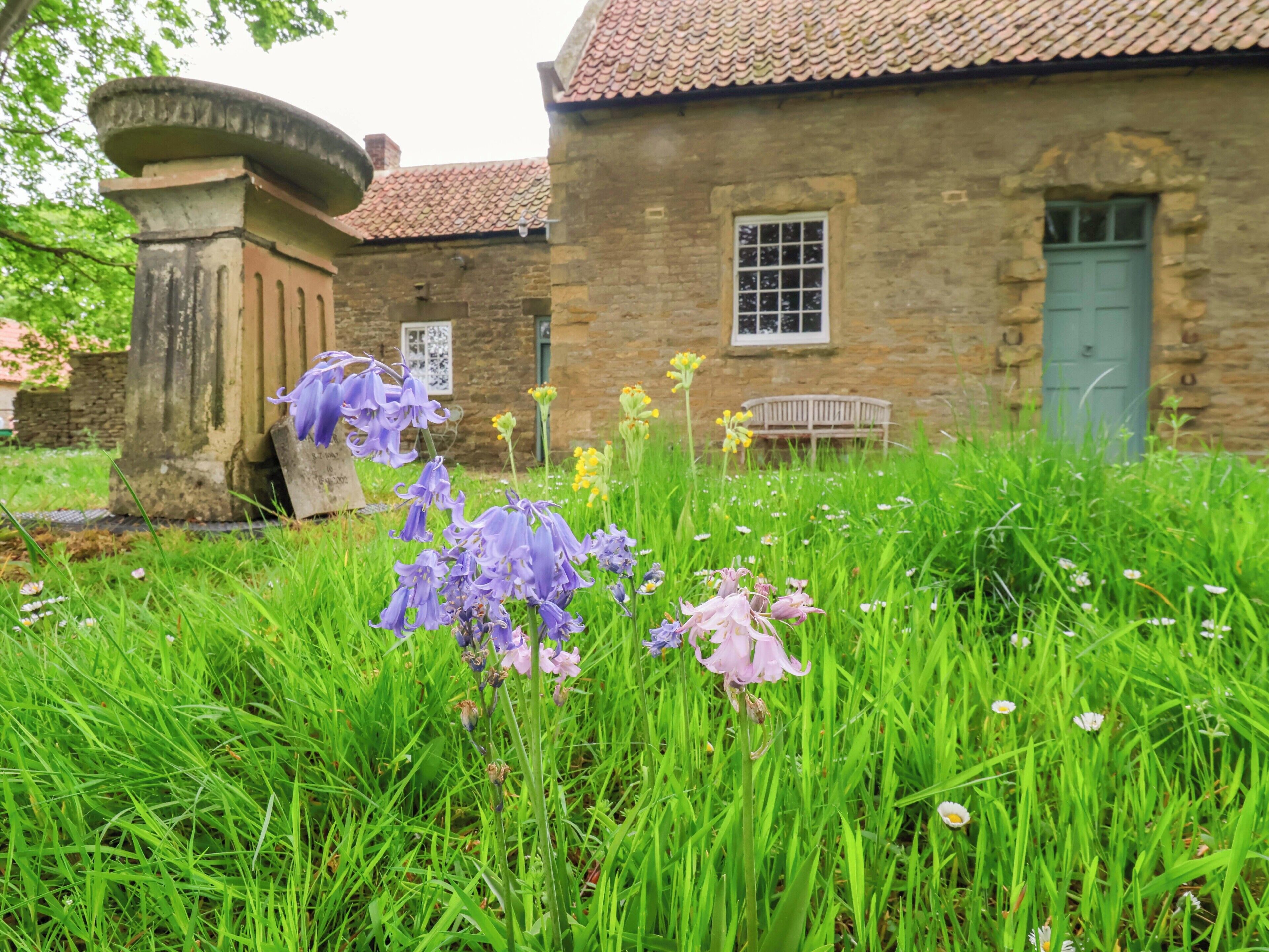 A stone building with a tiled roof, a bench, and a grassy area with flowers.
