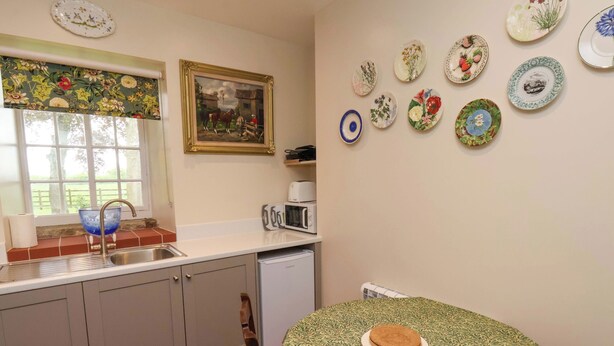 A kitchen with a sink, a window with a view, a microwave, and a toaster. There are plates on the wall and a chair in the corner. - The Gardener's Cottage, Low Hall (Scarborough)