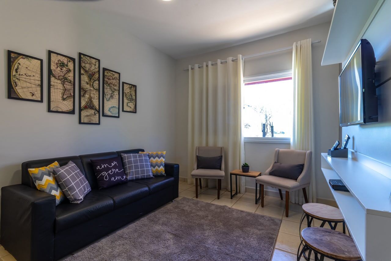 Una sala de estar moderna con un sofá de cuero negro, dos sillones, una mesa de centro, un televisor de pantalla plana y un ventanal con cortinas.