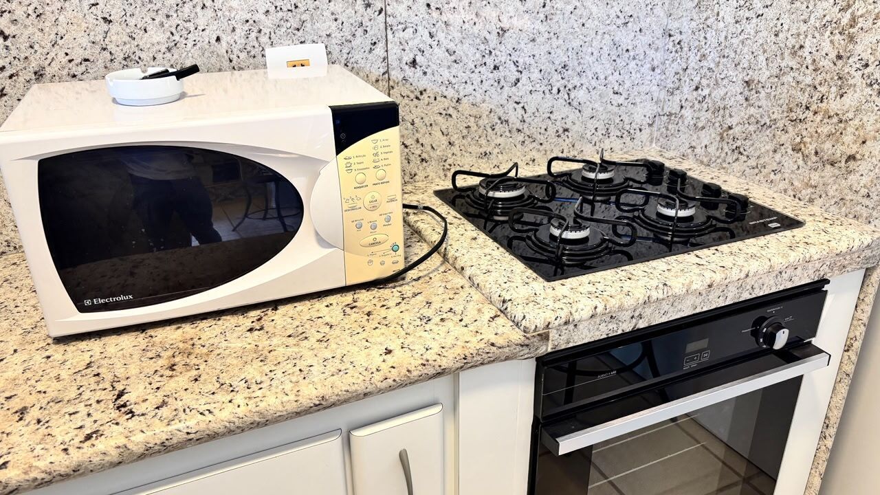 Cocina con microondas y estufa a gas sobre una encimera de granito, armarios blancos y horno de acero inoxidable.