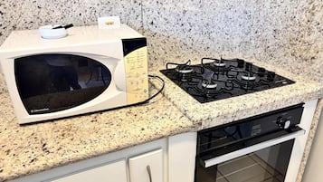 Cocina con microondas y estufa a gas sobre una encimera de granito, armarios blancos y horno de acero inoxidable.