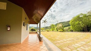 Un espacio al aire libre techado, con extintor, suelo de baldosas y vista a un paisaje verde con árboles y colinas.