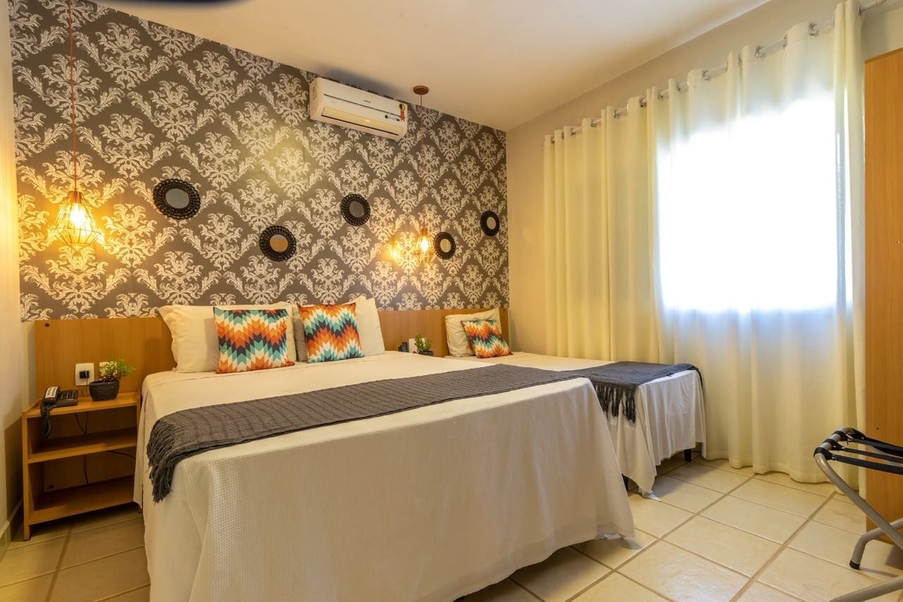 Habitación de hotel con una cama grande, dos mesitas de noche, un aire acondicionado y una ventana con cortinas.