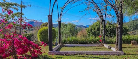 Um jardim com um gazebo, um pequeno lago e uma árvore florida em tons de rosa.