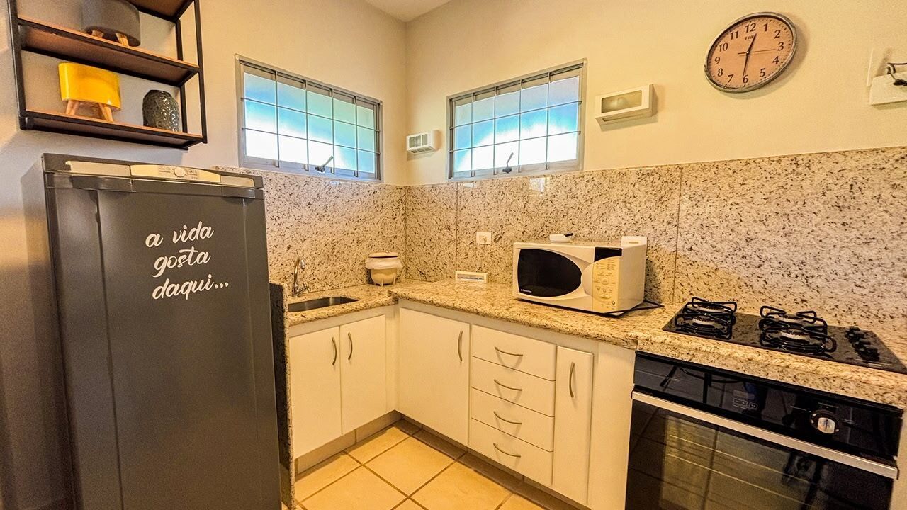 Cozinha com bancadas de granito, armários brancos, micro-ondas embutido, fogão e geladeira com uma frase motivacional.