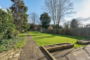 A backyard with a stone pathway, a wooden raised garden bed, and a wooden fence. - Spacious 3-Bedroom Home in Watford - Pass the Keys (Watford)