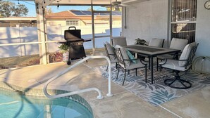 Un patio cubierto con piscina, una parrilla y una zona de comedor con sillas y mesa.