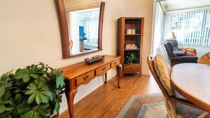 Una habitación con escritorio de madera, un espejo grande, una estantería, un sofá y una planta en maceta.