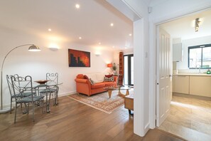 Ein Wohnzimmer mit einer Couch, einem Esstisch mit Stühlen, einer Küchenzeile und einer Tür zu einem anderen Raum.