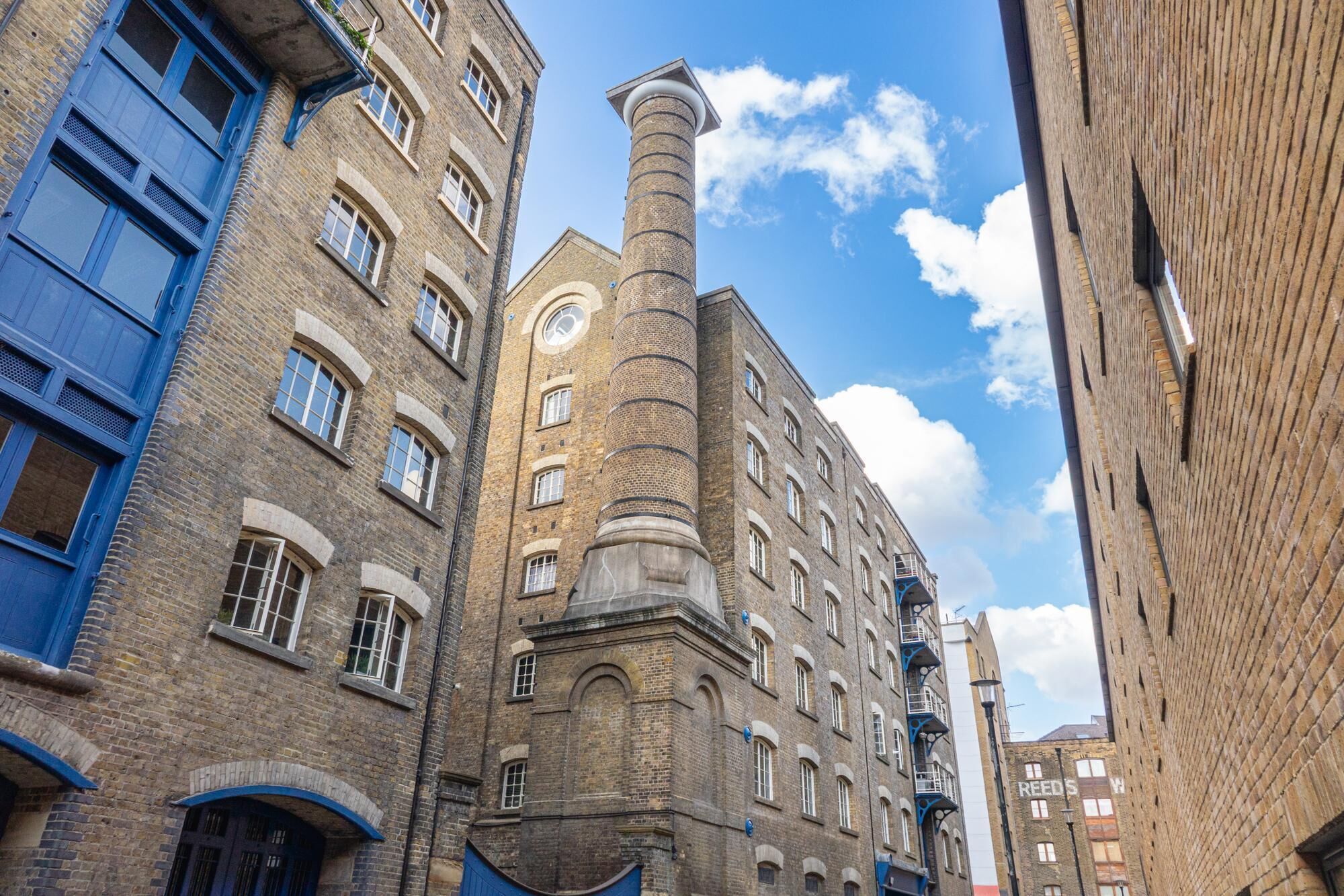 Une rue étroite bordée de bâtiments historiques en briques, dont l’un est surmonté d’une tour imposante et l’autre possède des portes bleues.