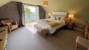Ein Schlafzimmer mit Bett, Stuhl, Nachttisch, Lampe und Blick ins Freie.