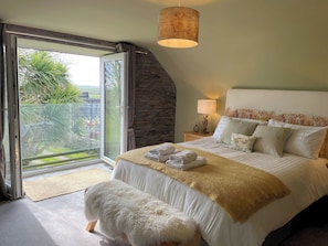 A bedroom with a large bed, a nightstand, a lamp, a fluffy rug, and a view of greenery outside.