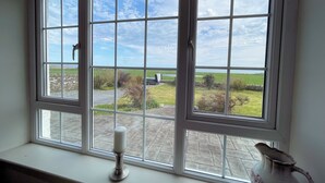 Ein Fenster mit Blick auf eine ländliche Landschaft, eine Kerze auf einem Fensterbrett und eine Vase auf dem Fensterbrett.