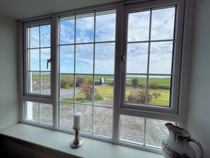 A window with a view of a rural landscape, a candle on a windowsill, and a vase on the windowsill.