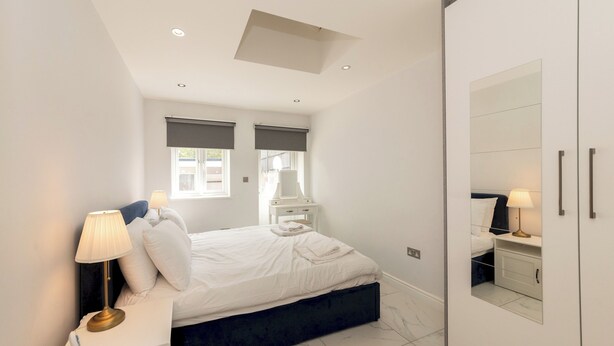 A bedroom with a bed, bedside tables, a nightstand, a mirror, and a wardrobe. - Modern House with AC 4 Parking & Transport Links - Pass the Keys (Reading)