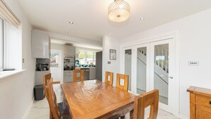 A dining area with a wooden table and chairs, a kitchen in the background, and a staircase leading to another floor. - Modern House with AC 4 Parking & Transport Links - Pass the Keys (Reading)