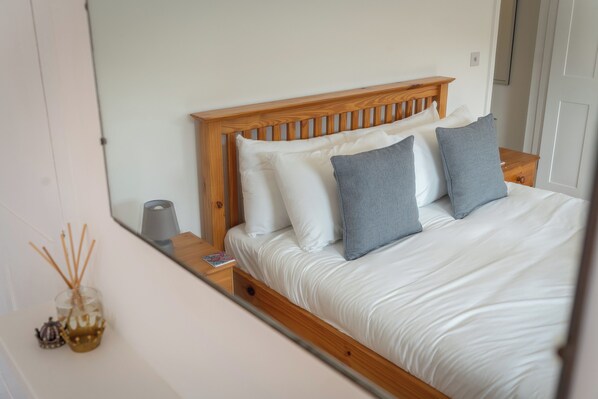 A bedroom with a wooden headboard, white bedding, and a bedside table with a lamp.