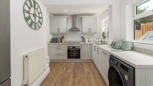 A modern kitchen with white cabinets, a built-in oven, a washing machine, and a large green clock on the wall. - Beautiful, newly refurbished Victorian townhouse - Pass the Keys (Windsor)