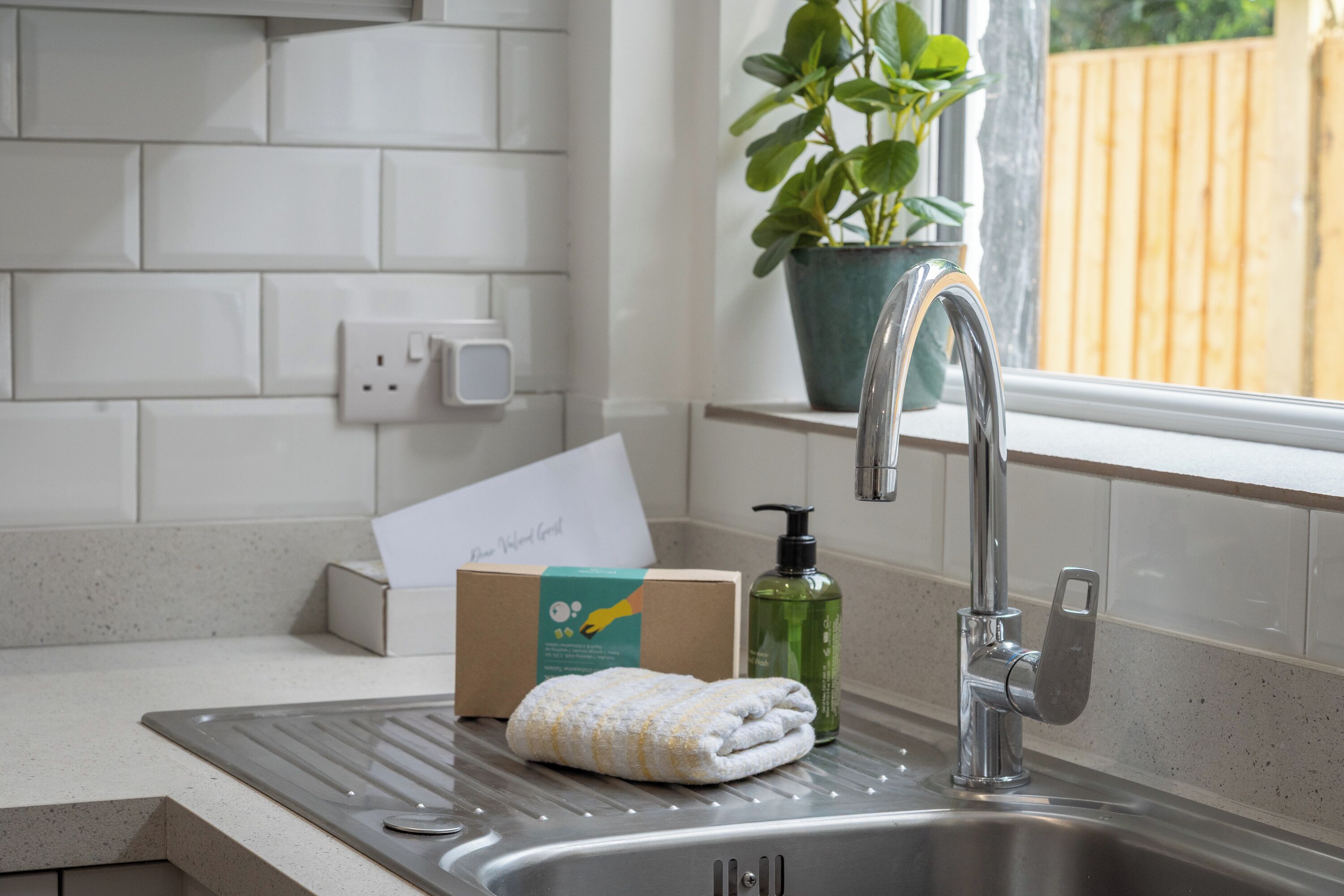 A kitchen sink with a faucet, a towel, a soap dispenser, and a card on the counter.