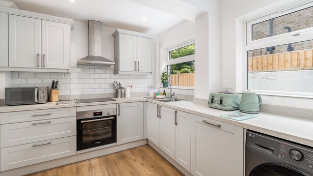 A modern kitchen with white cabinets, a built-in oven, a dishwasher, and a window with a view of greenery. - Beautiful, newly refurbished Victorian townhouse - Pass the Keys (Windsor)