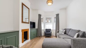 A living room with a green cabinet, a fireplace, a grey sofa, a grey armchair, and a television. - Beautiful, newly refurbished Victorian townhouse - Pass the Keys (Windsor)