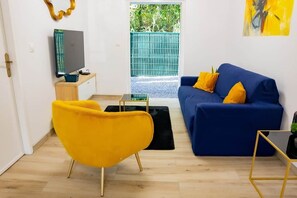 A living room with a blue sofa, yellow armchair, and a flat-screen TV on a wooden stand.