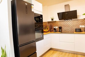 A modern kitchen with a stainless steel refrigerator, built-in oven, microwave, and a flat-screen TV.