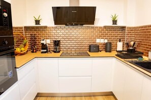 A compact kitchen with white cabinets, a brick backsplash, a built-in oven, a microwave, a coffee maker, and a TV above the stove. - Aiméelie Tropical Lodge: Pool & Close to Rivers (Lamentin)