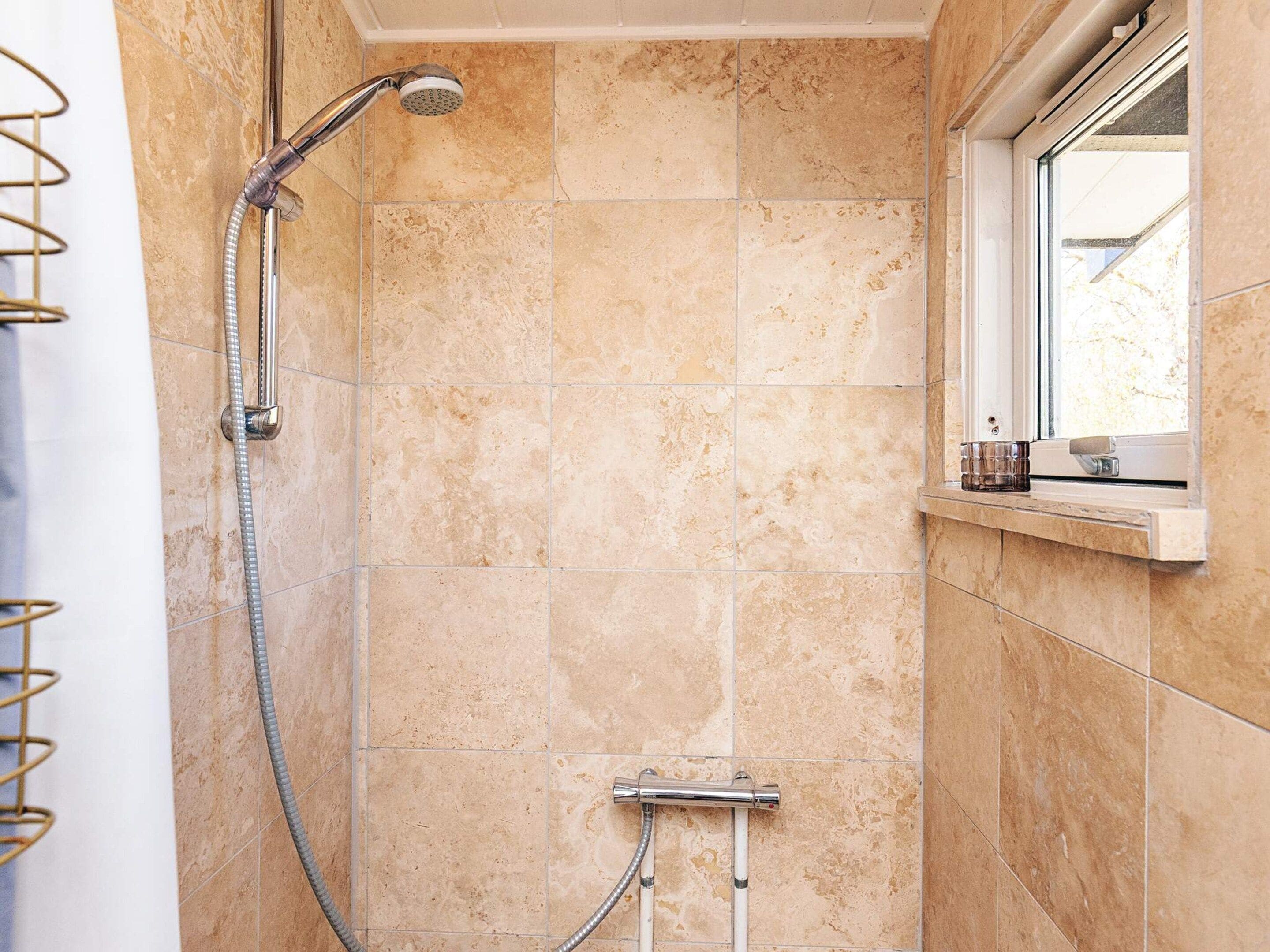 Une douche équipée d’un pommeau de douche à main et d’un robinet mural, le tout recouvert de carreaux de couleur beige.
