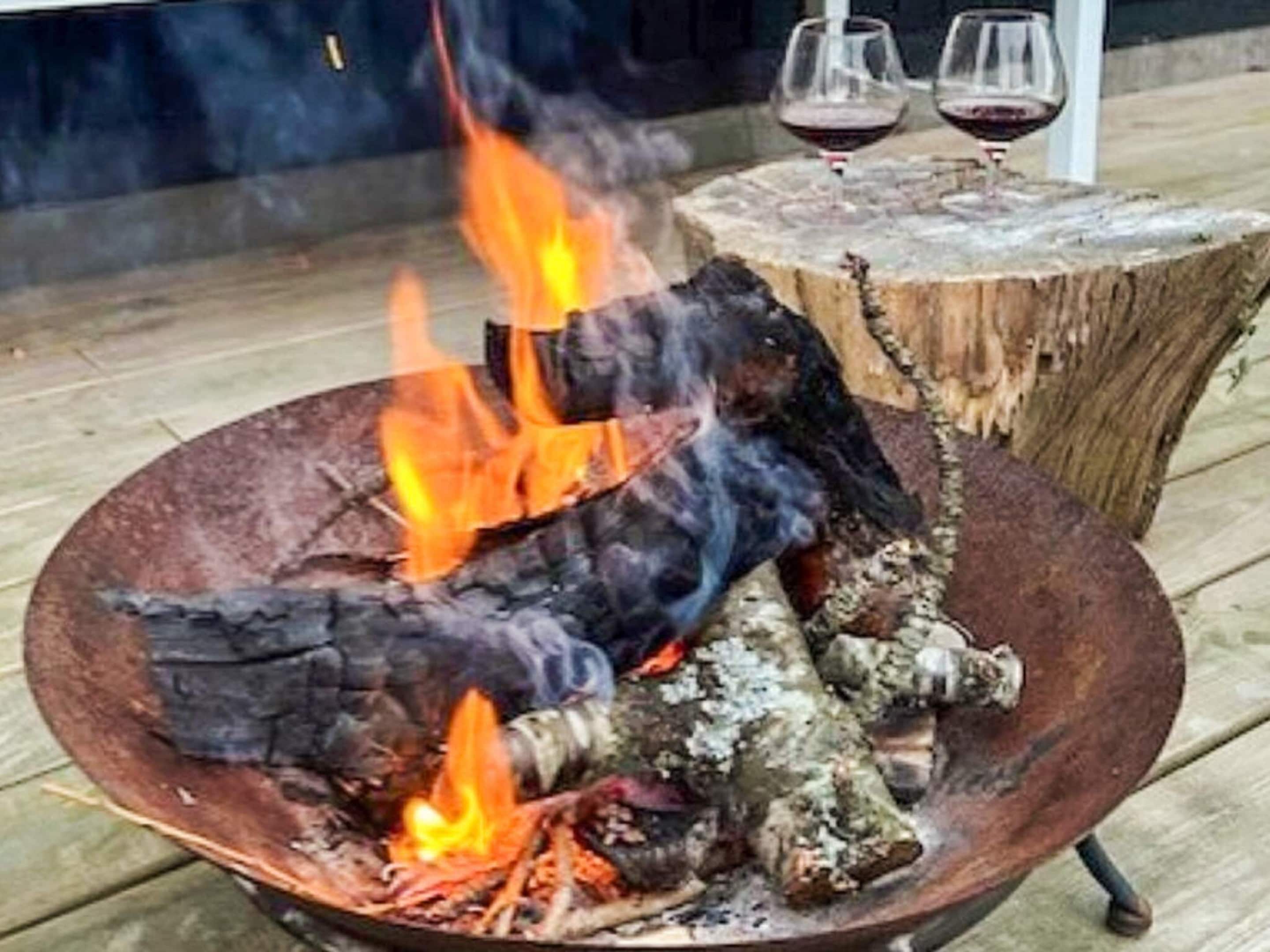Un hogar de leña con troncos y llamas, rodeado por una terraza de madera.