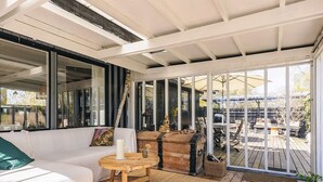 A covered patio with a sofa, a round wooden table, and a large window. - 4 Star Holiday Home in Graested (Graested)