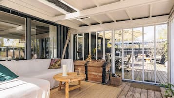 A covered patio with a sofa, a round wooden table, and a large window.