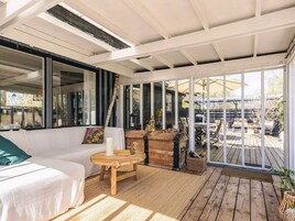 Un patio techado con un sofá, una mesa redonda de madera y un ventanal grande.