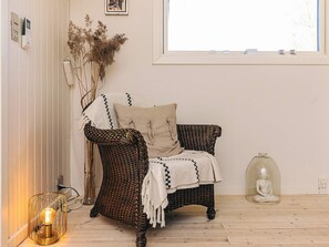 A wicker chair with a cushion, a glass vase with dried plants, a clear glass sculpture, and a wall-mounted light fixture.
