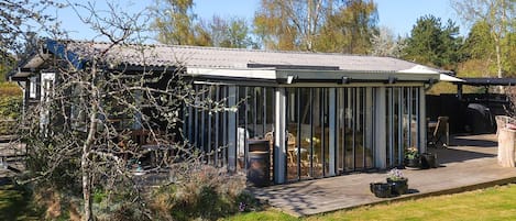Une maison moderne dotée d’une véranda en verre, d’une terrasse avec mobilier d’extérieur et d’une plateforme en bois.