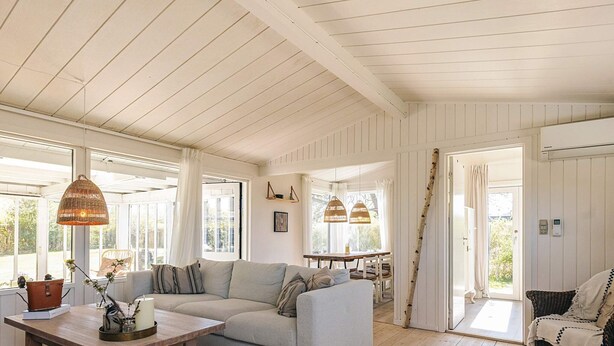 A spacious living area with a sofa, a wooden coffee table, wicker chairs, and a dining table. - 4 Star Holiday Home in Graested (Graested)