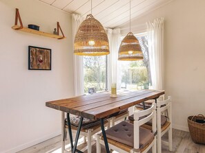 A dining area with a wooden table, white chairs, wicker pendant lights, a picture on the wall, and a window with curtains.