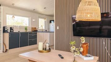 A modern kitchen with a TV, wooden cabinets, and a dining area with a table, vase, and remote control.